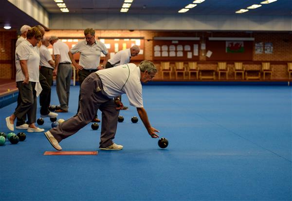 A bowler delivers a bowl, with the Welsh flag on the wall behind.